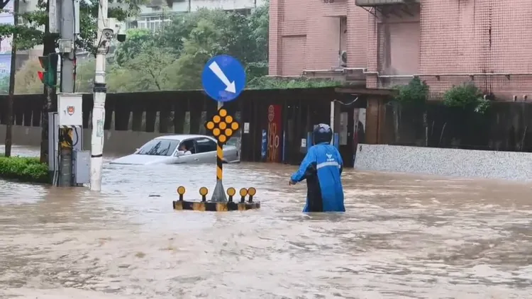 基隆市4日上午強降雨，導致大武崙溪溢流至基金一路沿線。一輛轎車冒險涉水卻拋錨，新崙里長林金龍（藍色雨衣）見狀上前協助，將年長駕駛攙扶至路旁。中央社（新崙里長林金龍提供）