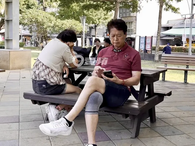 劉尚謙（右）和熟女愜意在建成公園滑手機。特勤中心攝