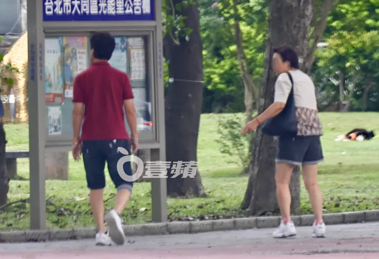 劉尚謙（左）帶著紅粉知己走進建成公園，不忘觀看里辦公室公告欄。特勤中心攝