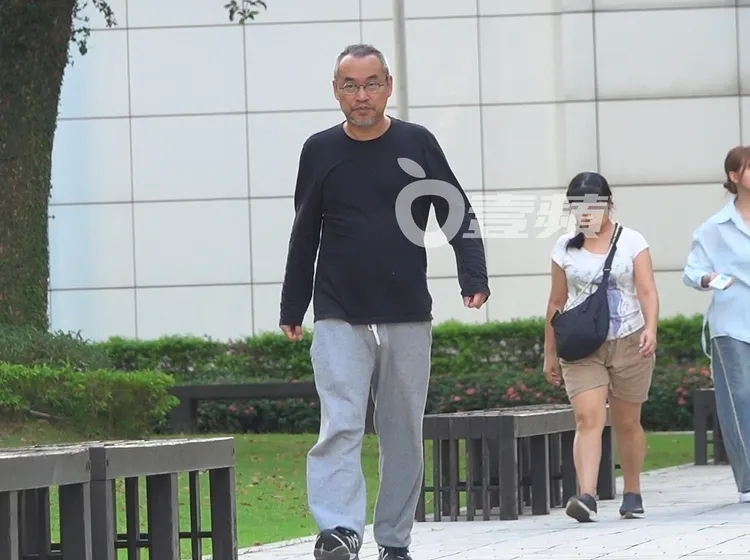 黃立成戴眼鏡，身穿深色薄長袖、配灰色棉褲、踩球鞋，打扮休閒。特勤中心攝