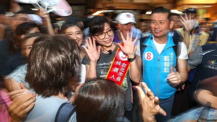 蔣萬安夫人石舫亘（中）、台北市議會議長戴錫欽（右藍背心者）今天到永春市場掃街拜票，石舫亘比出5號手勢，籲請民眾支持蔣萬安連任續拚市政。中央社